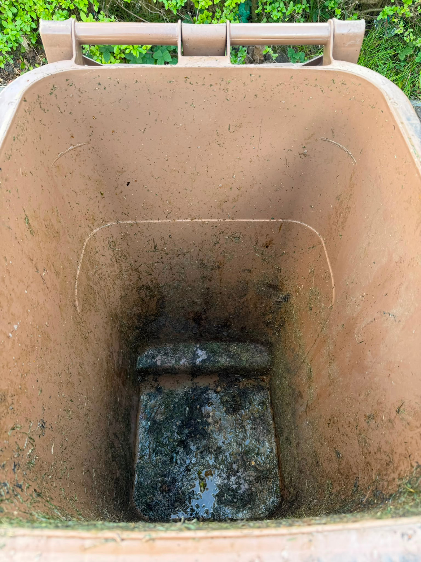 Inside of a brown garden waste wheelie bin caked with grass, mould and liquid waste before cleaning
