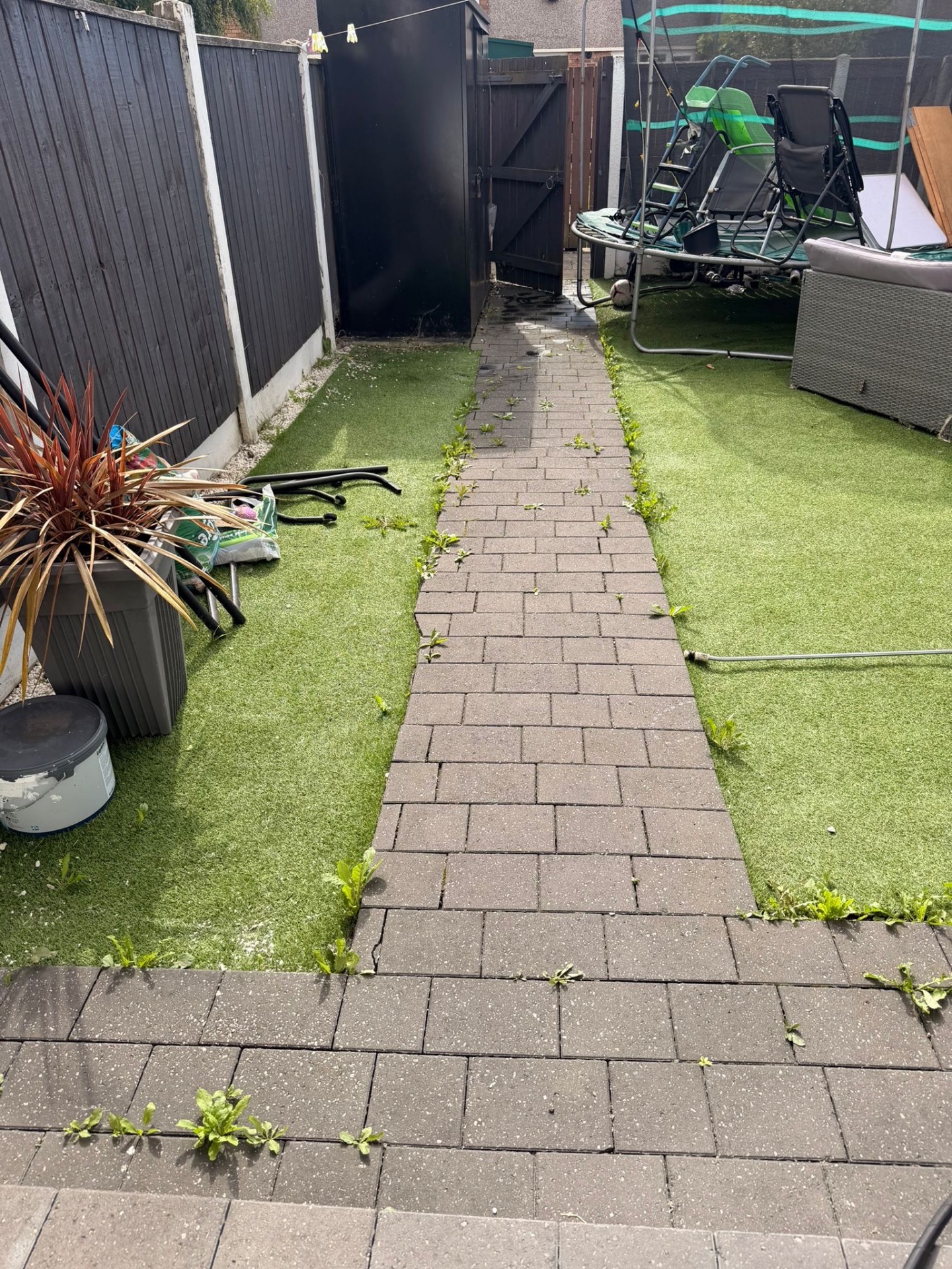 Weedy, dirty block paved garden path beside an artificial lawn before pressure washing