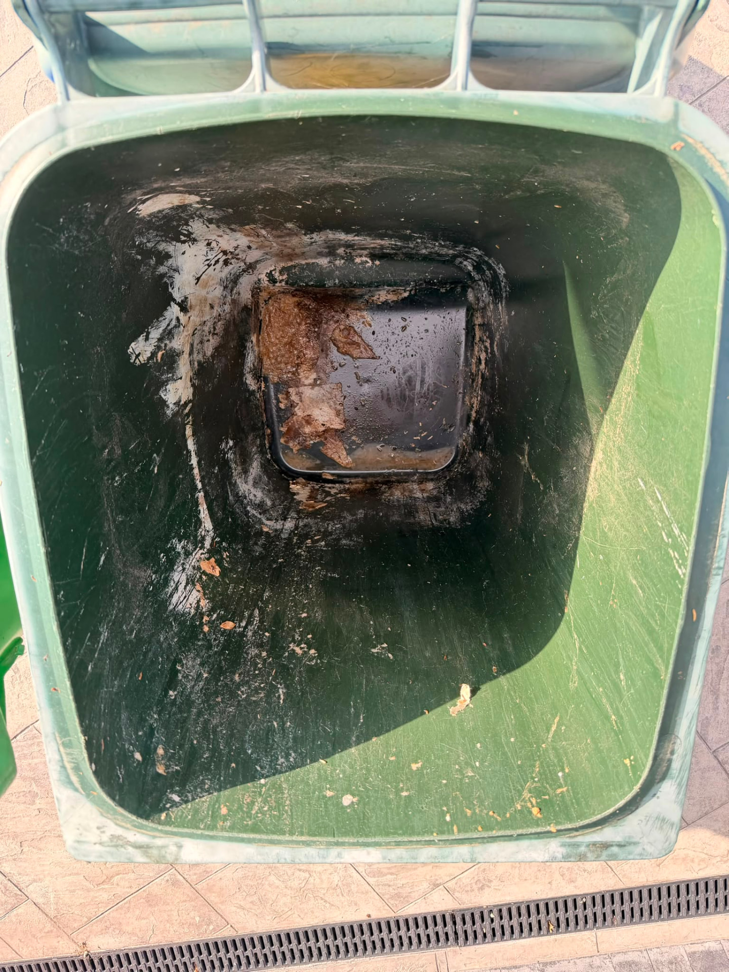Inside of a green wheelie bin heavily stained with black grime and sludge before cleaning